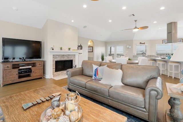 living room with light wood-type flooring, lofted ceiling, ceiling fan, and a stone fireplace