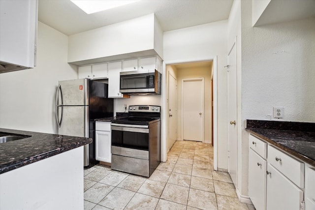 kitchen with light tile patterned floors, stainless steel appliances, dark stone counters, and white cabinets