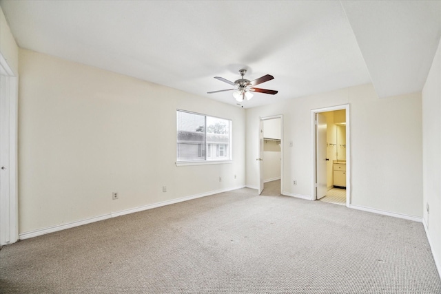 unfurnished bedroom with ensuite bathroom, a spacious closet, light colored carpet, a closet, and ceiling fan