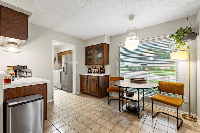 kitchen featuring pendant lighting, stainless steel fridge, dark brown cabinets, a textured ceiling, and separate washer and dryer