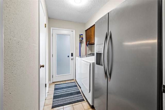 clothes washing area featuring cabinets, light tile patterned flooring, washing machine and clothes dryer, and a textured ceiling