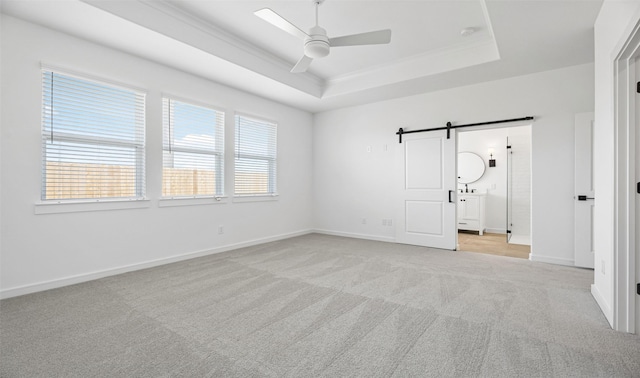 unfurnished room featuring ceiling fan, a tray ceiling, crown molding, a barn door, and light carpet