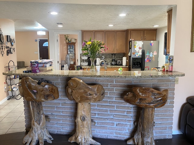 kitchen with stainless steel refrigerator with ice dispenser, light tile patterned flooring, stone countertops, a textured ceiling, and kitchen peninsula