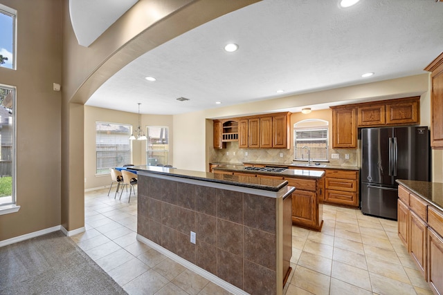 kitchen featuring sink, stainless steel refrigerator, backsplash, a kitchen island, and light tile patterned flooring