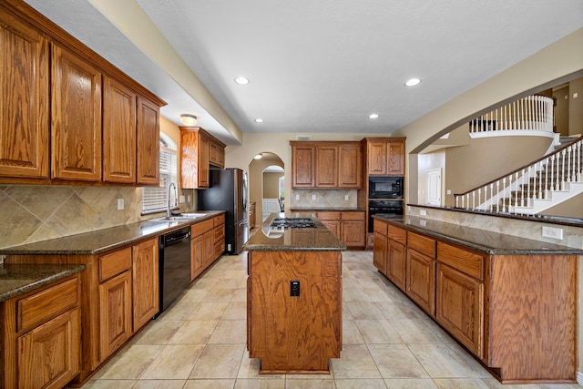 kitchen featuring a kitchen island, sink, dark stone counters, and black appliances