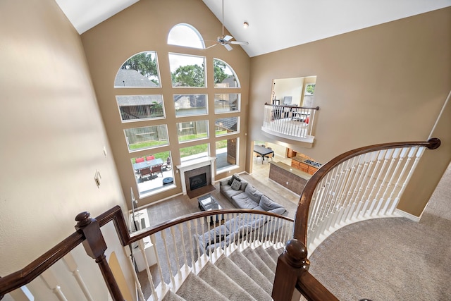 staircase featuring a tiled fireplace, high vaulted ceiling, and ceiling fan