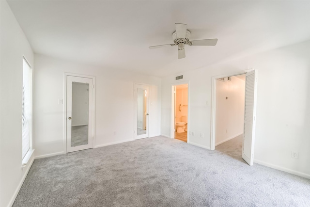 unfurnished bedroom featuring multiple windows, light colored carpet, ceiling fan, and ensuite bathroom