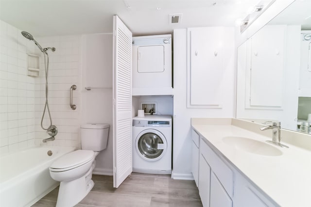 full bathroom with tiled shower / bath, stacked washer and dryer, vanity, hardwood / wood-style flooring, and toilet