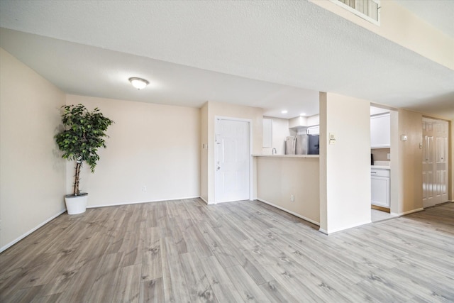 unfurnished living room with light wood-style flooring, baseboards, and a textured ceiling