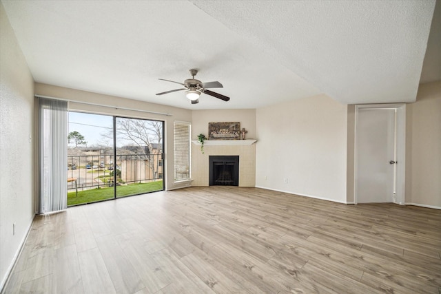 unfurnished living room featuring a textured ceiling, ceiling fan, a fireplace, wood finished floors, and baseboards