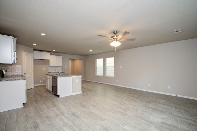 kitchen featuring white cabinetry, a center island with sink, dishwasher, light stone countertops, and backsplash