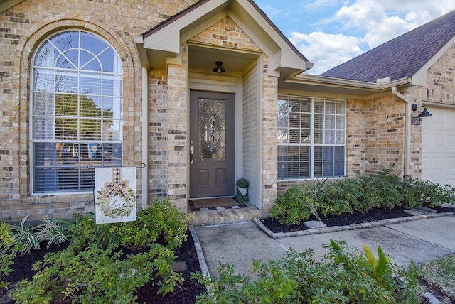 view of exterior entry featuring a garage, brick siding, and a shingled roof