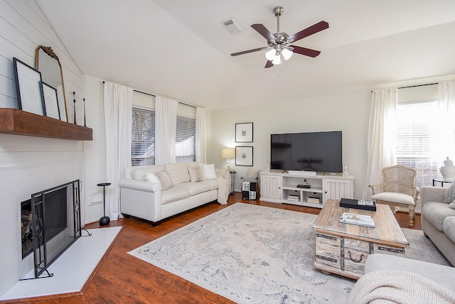 living area featuring lofted ceiling, a fireplace, wood finished floors, visible vents, and a ceiling fan