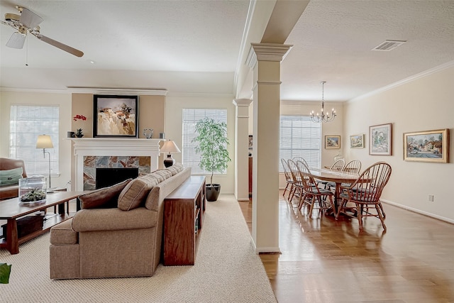 living area featuring a fireplace, visible vents, ornamental molding, wood finished floors, and ornate columns