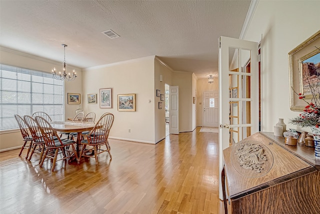 dining space featuring a textured ceiling, a chandelier, light wood-style flooring, and crown molding