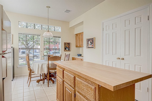 kitchen with decorative light fixtures, visible vents, light tile patterned flooring, a kitchen island, and wood counters