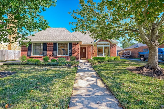 view of front of house featuring roof with shingles, a front yard, fence, and brick siding