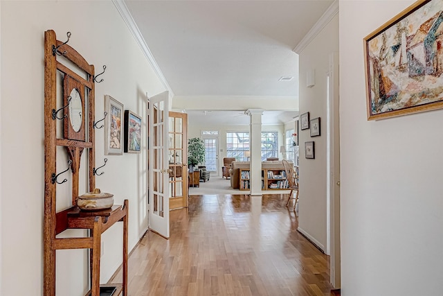 hallway with french doors, ornate columns, ornamental molding, light wood-type flooring, and baseboards