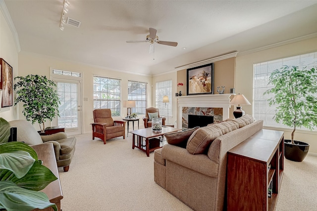 living room featuring ornamental molding, a stone fireplace, a wealth of natural light, and light colored carpet