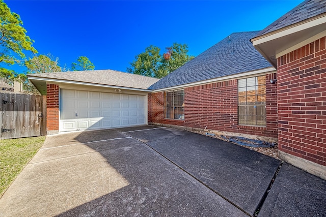 exterior space with driveway, a shingled roof, an attached garage, fence, and brick siding