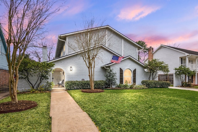 view of front of house with brick siding, a lawn, and fence