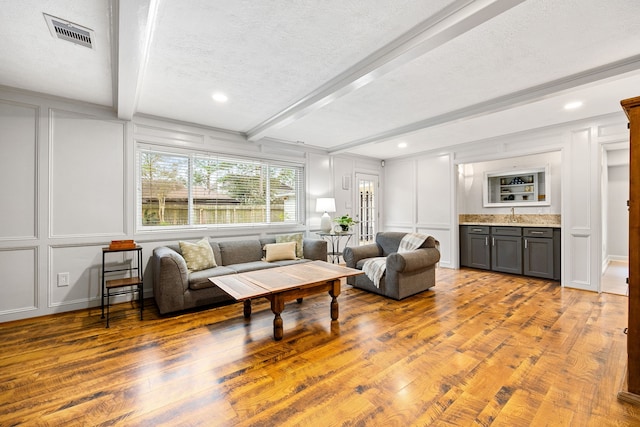 living room featuring visible vents, wood finished floors, beam ceiling, and a decorative wall