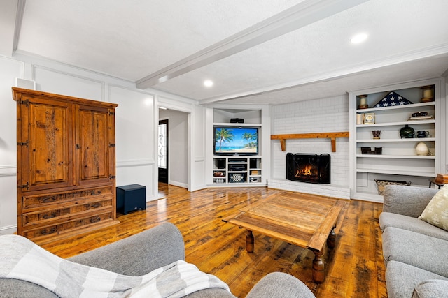 living room with built in shelves, a brick fireplace, beam ceiling, and wood finished floors