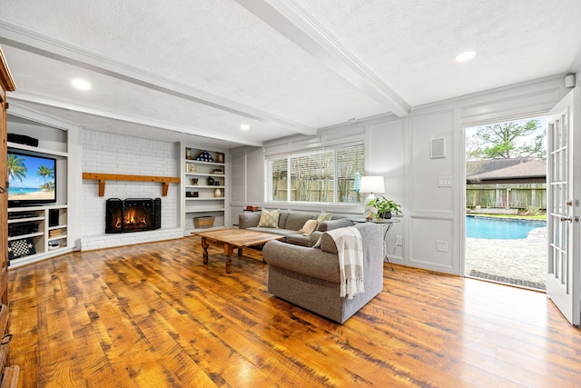 living area with a textured ceiling, a decorative wall, a fireplace, built in features, and beamed ceiling