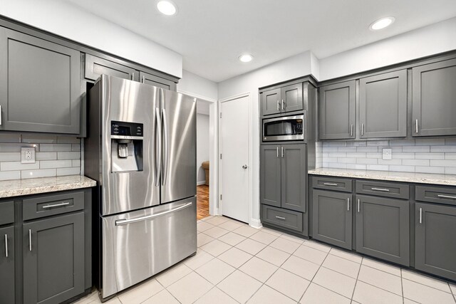 kitchen with appliances with stainless steel finishes, light stone countertops, light tile patterned flooring, backsplash, and recessed lighting