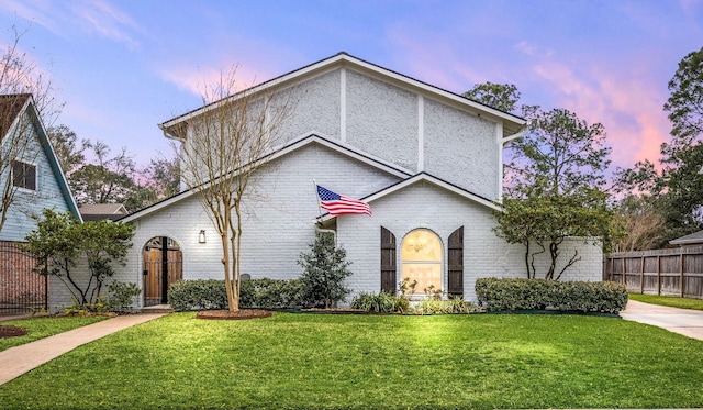 view of front of property featuring brick siding, fence, and a front lawn