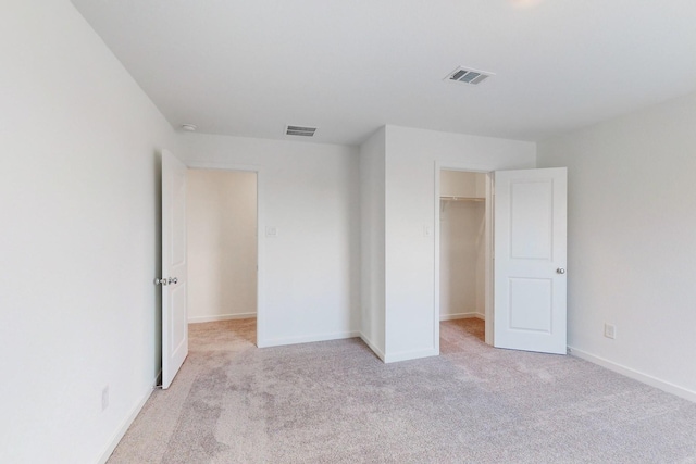 unfurnished bedroom with a walk in closet, light carpet, and a closet