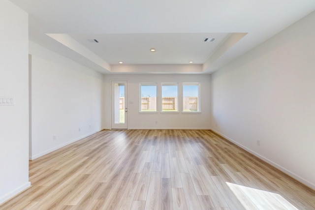 empty room featuring a tray ceiling and light wood-type flooring