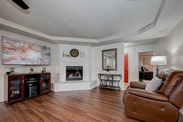 living room with a textured ceiling, a fireplace, a tray ceiling, and wood finished floors