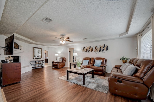 living area with a tray ceiling, a brick fireplace, wood finished floors, and visible vents