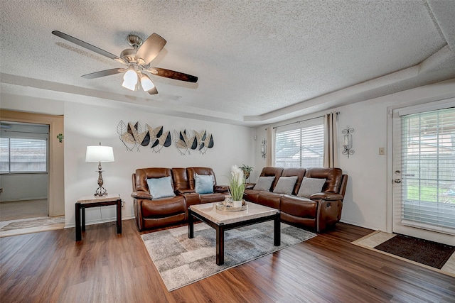 living room with ceiling fan, a textured ceiling, a raised ceiling, and wood finished floors