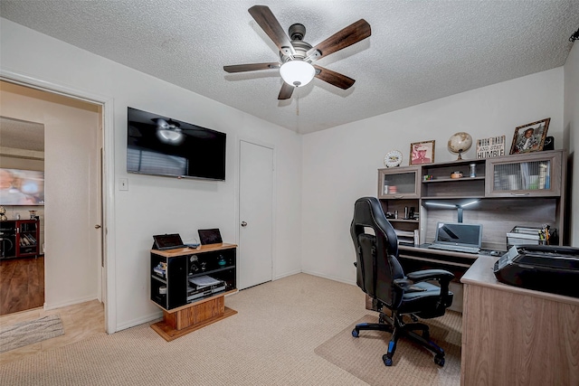 office area featuring baseboards, a ceiling fan, a textured ceiling, and light colored carpet