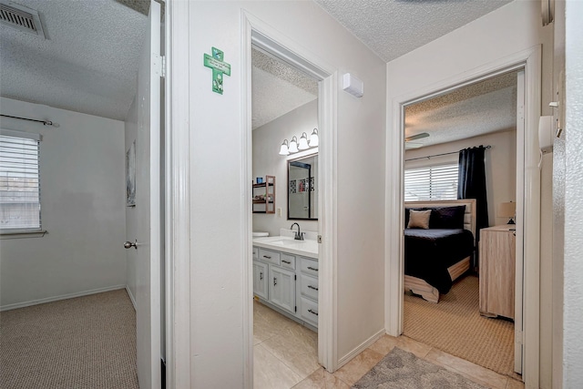 hallway with a textured ceiling, a sink, visible vents, and light colored carpet