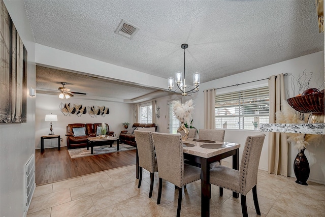 dining space with a textured ceiling, light tile patterned floors, ceiling fan with notable chandelier, and visible vents