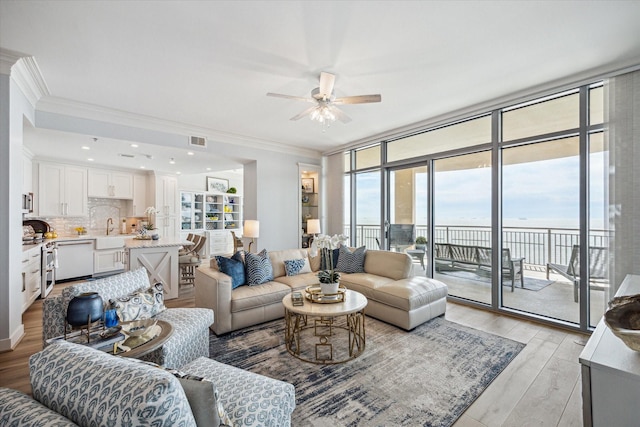 living room featuring crown molding, light wood-type flooring, visible vents, and a water view