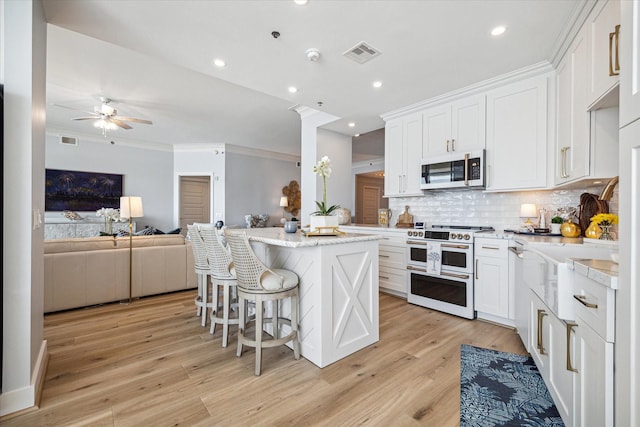 kitchen featuring white appliances, visible vents, a kitchen island, open floor plan, and white cabinetry