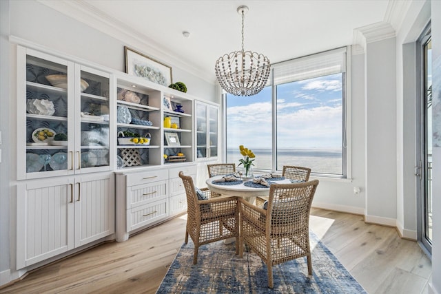 dining space with a water view, baseboards, ornamental molding, light wood-type flooring, and an inviting chandelier