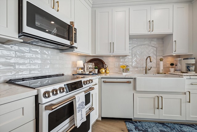 kitchen with white appliances, a sink, white cabinets, backsplash, and light stone countertops