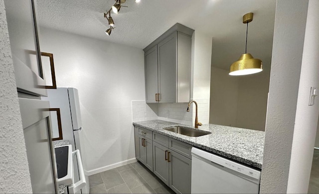 kitchen with gray cabinetry, a sink, tasteful backsplash, light stone countertops, and dishwasher