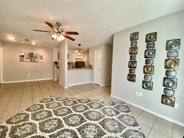 empty room with a textured ceiling, light tile patterned flooring, baseboards, and ceiling fan