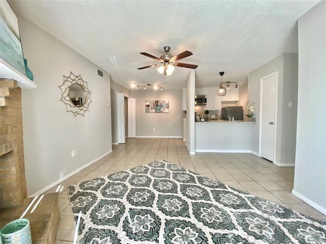 unfurnished living room featuring visible vents, baseboards, ceiling fan, light tile patterned flooring, and a textured ceiling