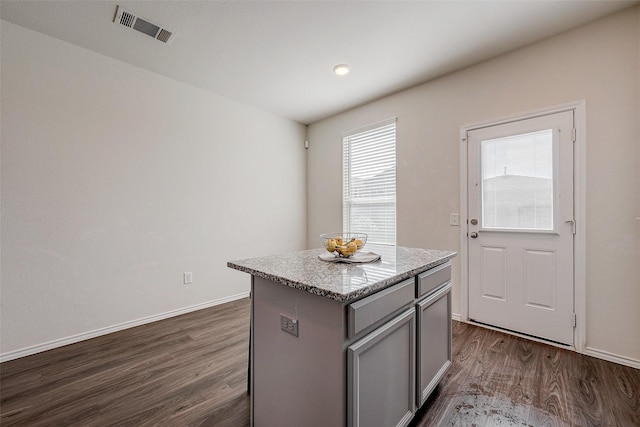 kitchen featuring light stone countertops, a center island, gray cabinetry, and dark wood-type flooring