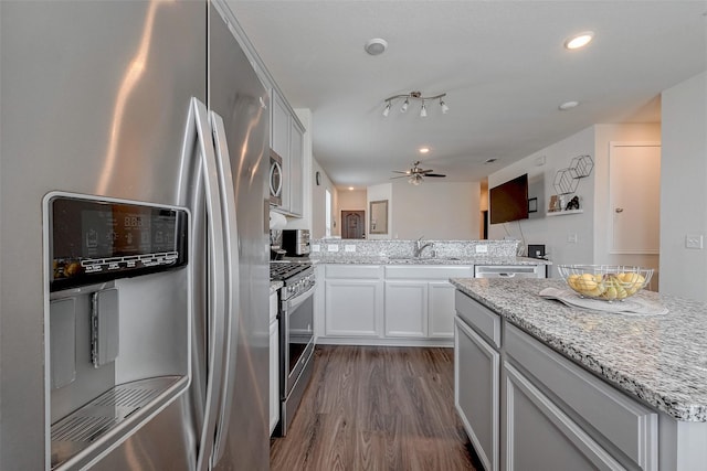 kitchen with dark wood-type flooring, light stone counters, appliances with stainless steel finishes, ceiling fan, and white cabinets