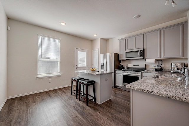 kitchen with sink, dark hardwood / wood-style flooring, a center island, light stone counters, and stainless steel appliances