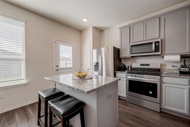 kitchen featuring light stone countertops, dark hardwood / wood-style floors, stainless steel appliances, and a center island