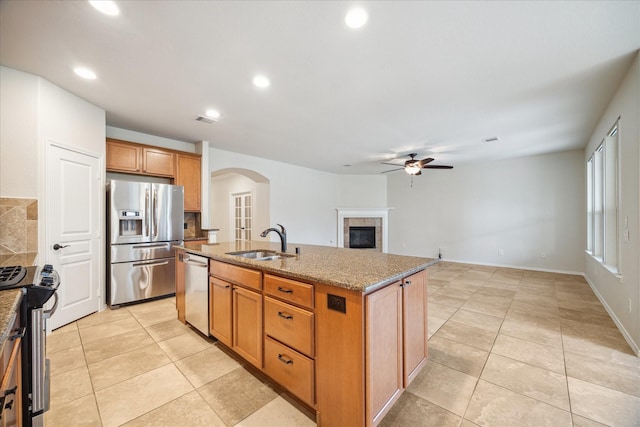 kitchen with a sink, light stone countertops, a tiled fireplace, stainless steel appliances, and a kitchen island with sink